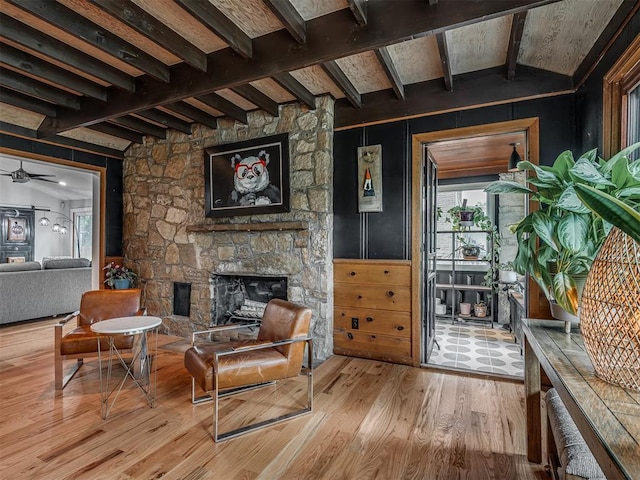 living area featuring a fireplace, ceiling fan, beamed ceiling, and wood finished floors
