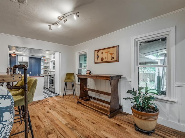 dining room featuring ornamental molding, a decorative wall, wood finished floors, and a wainscoted wall