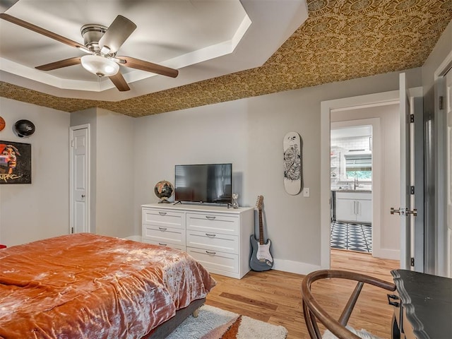 bedroom with ceiling fan, light wood-type flooring, a sink, a raised ceiling, and baseboards