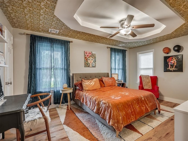 bedroom with a tray ceiling, visible vents, and wood finished floors