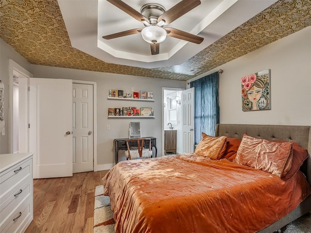 bedroom with light wood-type flooring, ceiling fan, and a tray ceiling