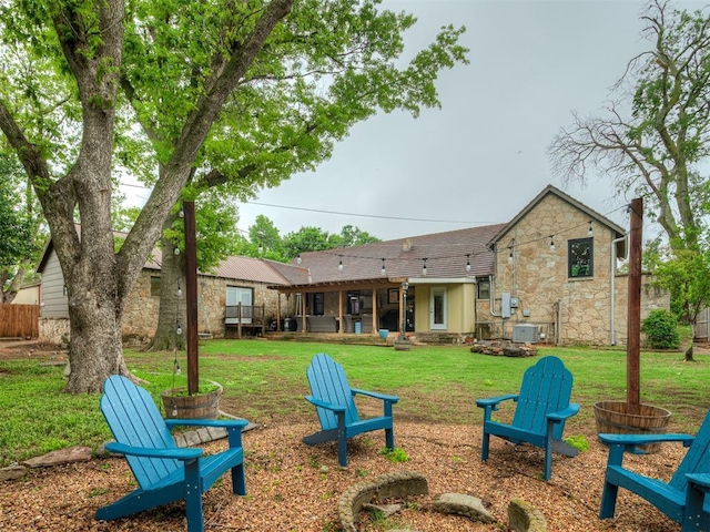 back of property featuring a lawn, an outdoor fire pit, central air condition unit, and stone siding