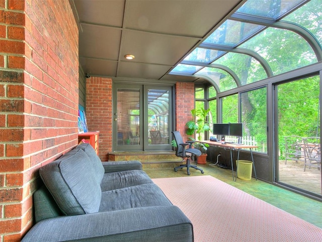 sunroom with a healthy amount of sunlight, concrete flooring, and brick wall