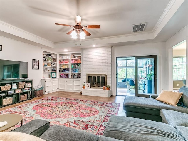 living room with a ceiling fan, visible vents, crown molding, wood finished floors, and a tray ceiling