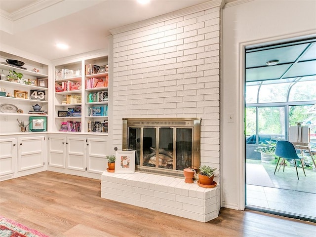 living area with crown molding, built in shelves, light wood finished floors, and a fireplace