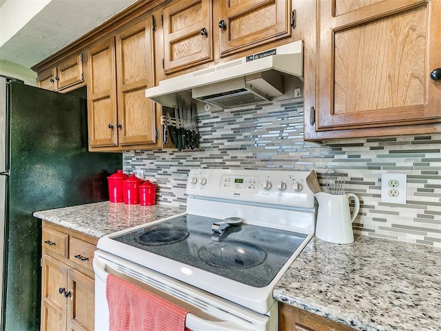 kitchen featuring brown cabinets, electric range, freestanding refrigerator, decorative backsplash, and under cabinet range hood