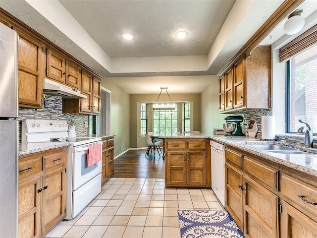 kitchen featuring decorative backsplash, light tile patterned floors, a peninsula, under cabinet range hood, and white appliances
