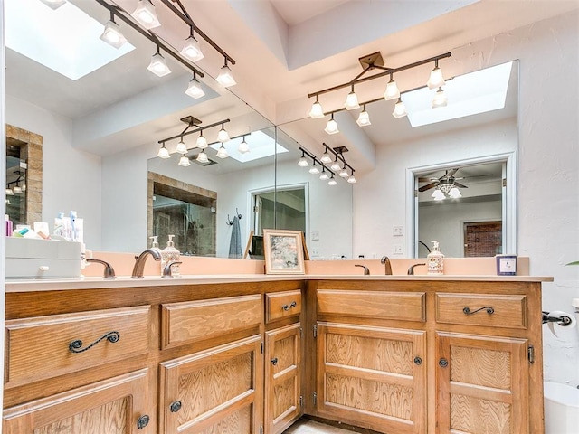 bathroom featuring track lighting, a sink, double vanity, a skylight, and a shower with door