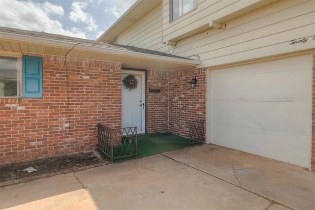 doorway to property featuring brick siding, driveway, and a garage