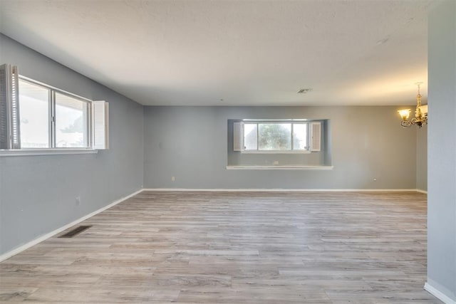 empty room featuring baseboards, visible vents, an inviting chandelier, and light wood-style flooring