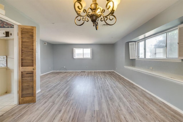 empty room featuring baseboards, visible vents, wood finished floors, and a chandelier