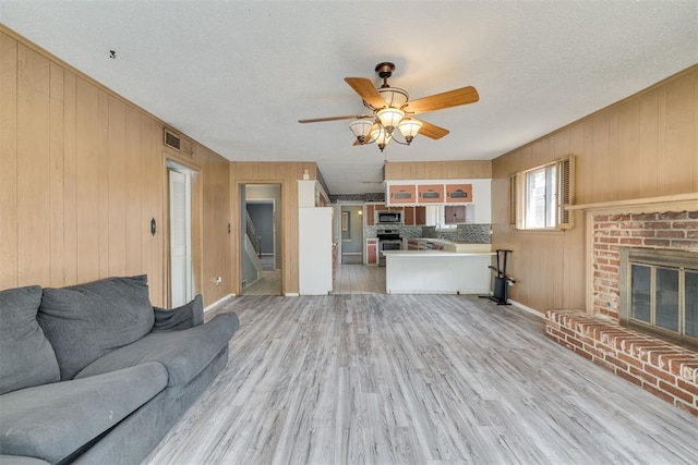 unfurnished living room with wooden walls, a ceiling fan, a brick fireplace, and visible vents
