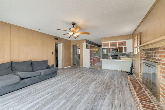 living room featuring visible vents, a fireplace, wooden walls, a textured ceiling, and a ceiling fan