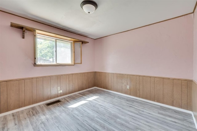 unfurnished room with visible vents, wood walls, wood finished floors, a wainscoted wall, and baseboards