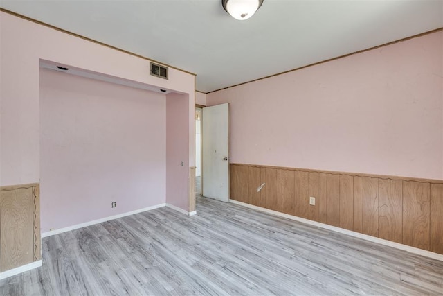 spare room with visible vents, wood finished floors, baseboards, wooden walls, and a wainscoted wall