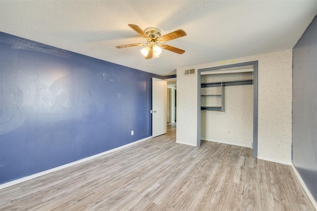 unfurnished bedroom with ceiling fan, a textured ceiling, wood finished floors, visible vents, and a closet
