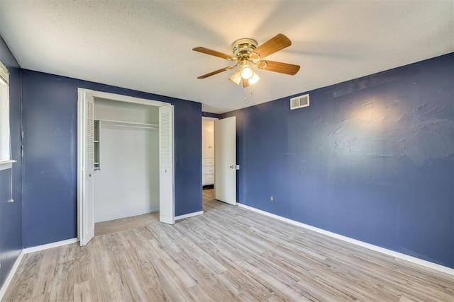 unfurnished bedroom featuring a textured ceiling, visible vents, baseboards, a closet, and light wood-style floors