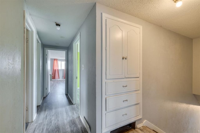 hallway featuring light wood-style floors, baseboards, and a textured ceiling