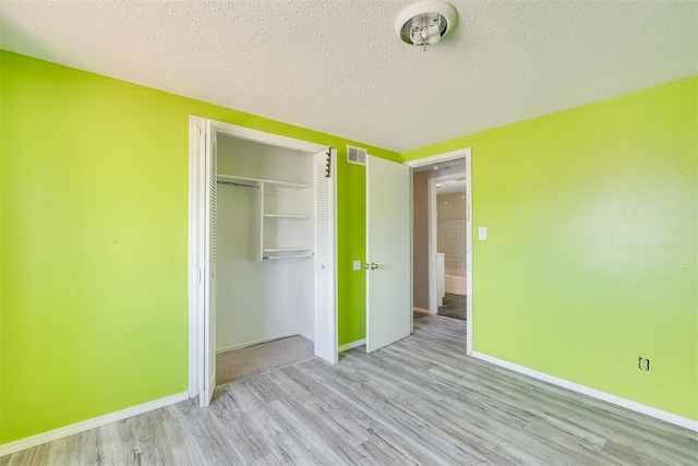 unfurnished bedroom featuring a textured ceiling, visible vents, wood finished floors, baseboards, and a closet
