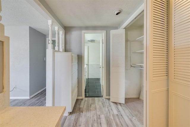 hallway featuring a textured ceiling, baseboards, and light wood-style floors