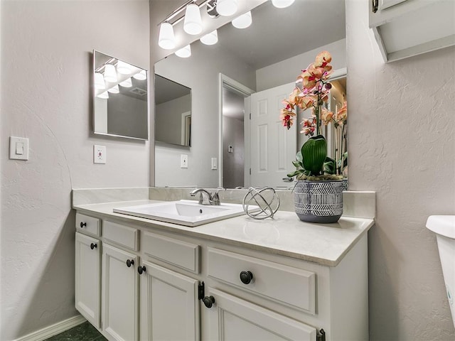 half bathroom with baseboards, vanity, and a textured wall