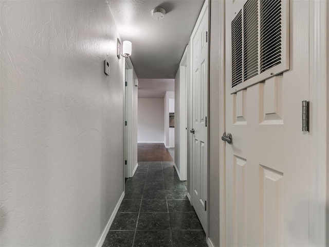corridor featuring baseboards, visible vents, and dark tile patterned floors