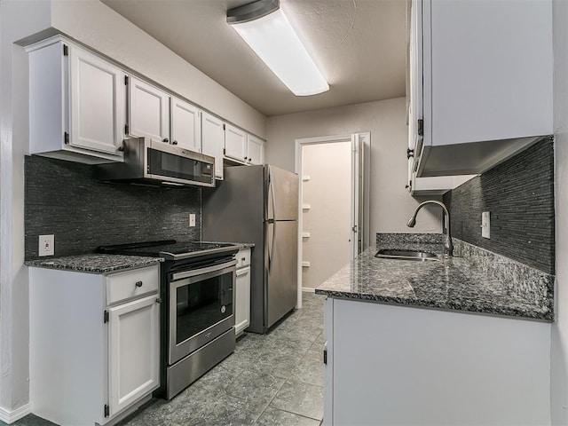 kitchen featuring a sink, stainless steel appliances, dark stone counters, backsplash, and white cabinetry