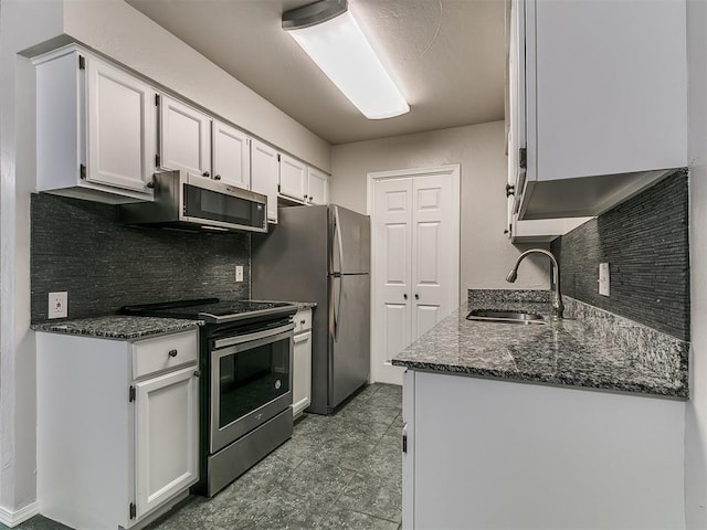 kitchen with a sink, dark stone counters, white cabinets, appliances with stainless steel finishes, and tasteful backsplash