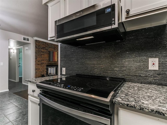 kitchen featuring stainless steel microwave, visible vents, backsplash, white cabinetry, and electric range oven