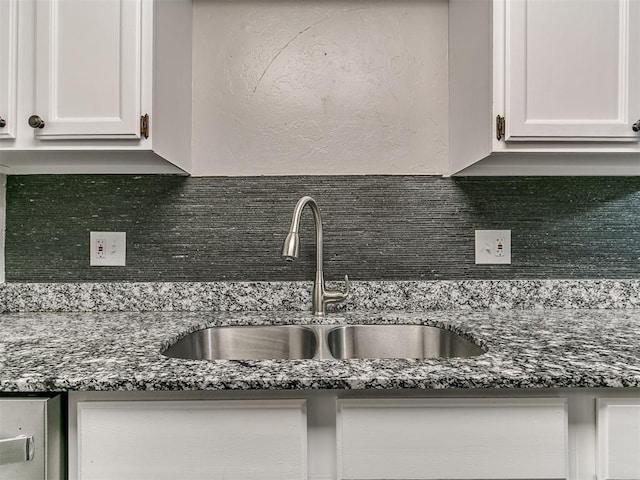 kitchen with dark stone counters, backsplash, white cabinetry, and a sink