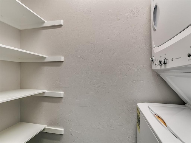 clothes washing area featuring stacked washer and clothes dryer, laundry area, and a textured wall