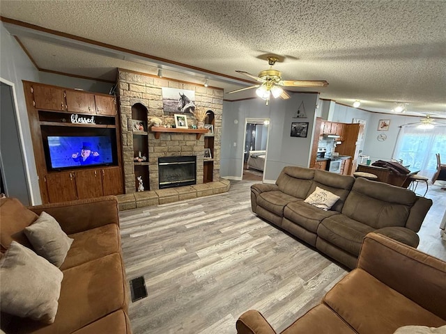 living room with light wood-type flooring, a ceiling fan, a textured ceiling, and a stone fireplace