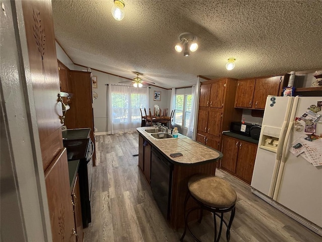 kitchen with wood finished floors, tile counters, brown cabinets, a sink, and black appliances