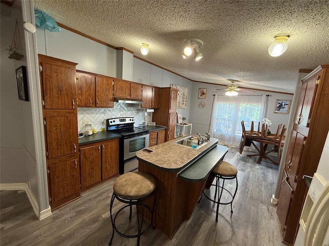 kitchen with stainless steel range with electric cooktop, dark wood finished floors, brown cabinetry, and ornamental molding