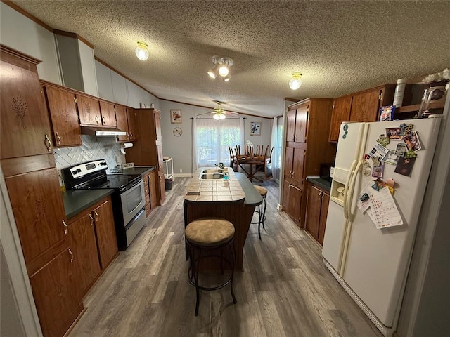 kitchen featuring wood finished floors, a kitchen island, white refrigerator with ice dispenser, under cabinet range hood, and stainless steel range with electric cooktop