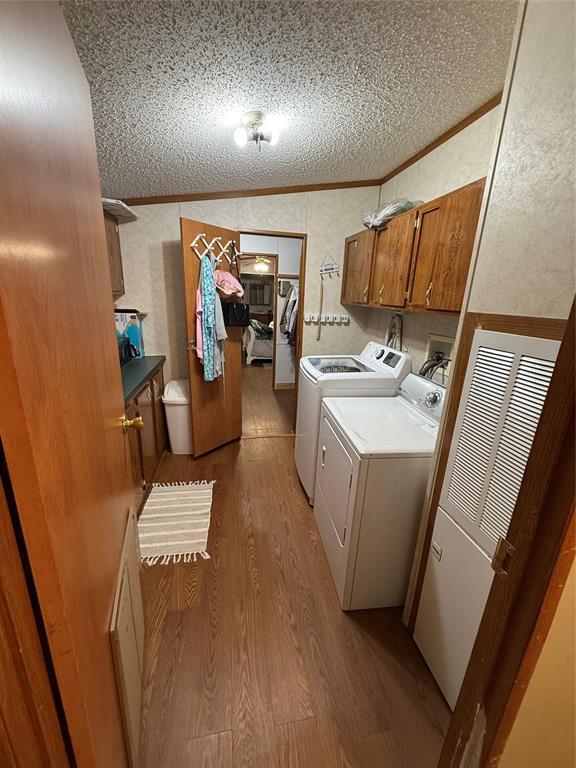 laundry area featuring cabinet space, a textured ceiling, ornamental molding, wood finished floors, and washing machine and dryer