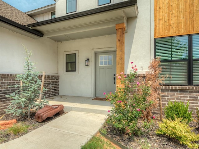 view of exterior entry with stucco siding and brick siding