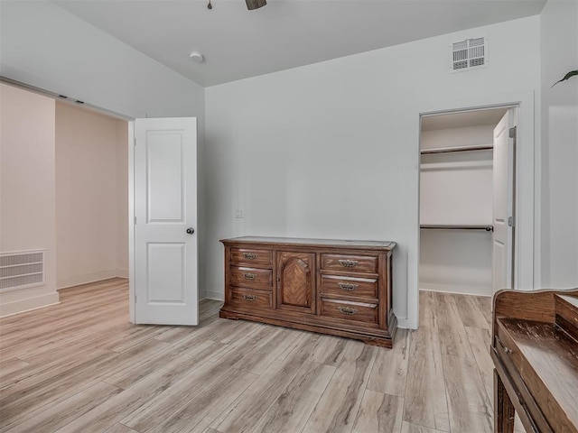 unfurnished bedroom with visible vents, baseboards, a walk in closet, and light wood-type flooring