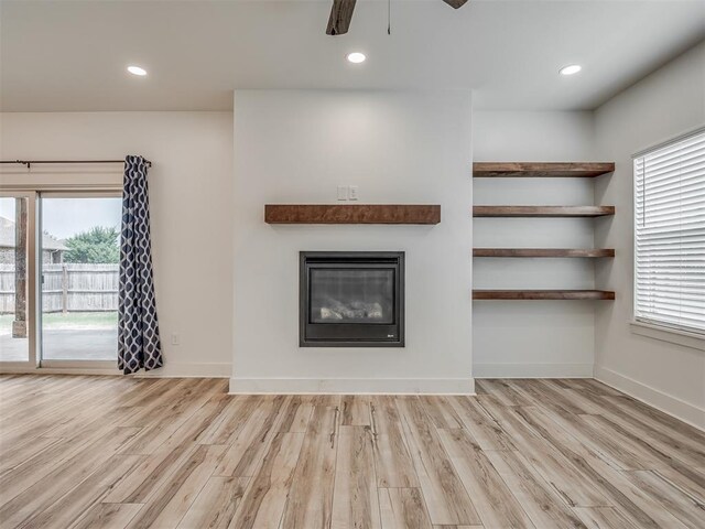unfurnished living room featuring a glass covered fireplace, a ceiling fan, wood finished floors, and a wealth of natural light