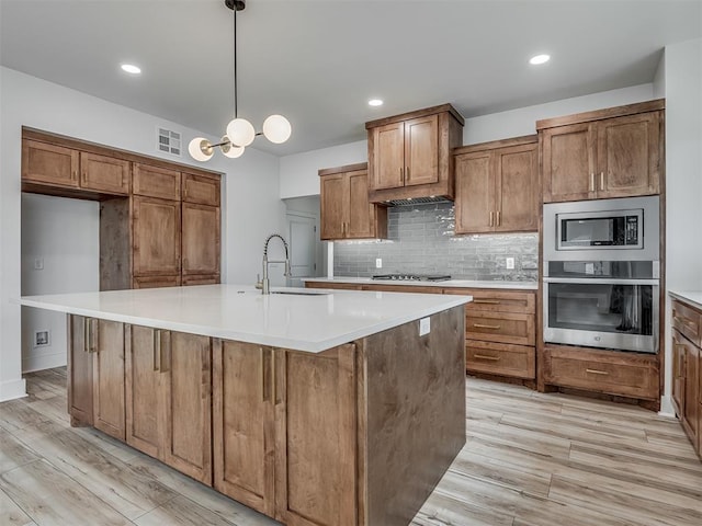 kitchen with visible vents, brown cabinets, a sink, light wood-style flooring, and stainless steel appliances