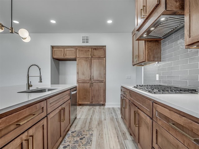 kitchen featuring brown cabinetry, range hood, a sink, stainless steel appliances, and light wood-style flooring