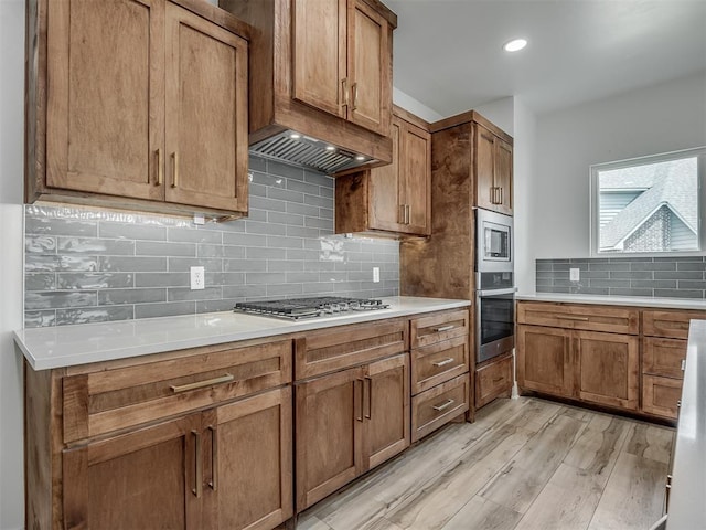 kitchen with brown cabinets, appliances with stainless steel finishes, light wood-style floors, light countertops, and backsplash