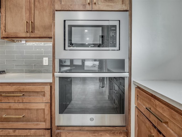 interior details featuring light countertops, stainless steel microwave, brown cabinets, and tasteful backsplash