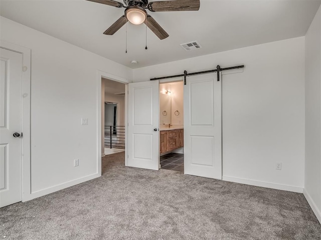 unfurnished bedroom featuring connected bathroom, a barn door, carpet floors, baseboards, and visible vents