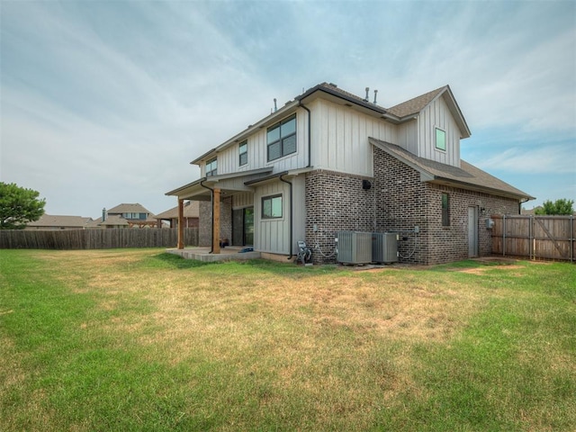 back of property with a fenced backyard, board and batten siding, central AC, and a yard