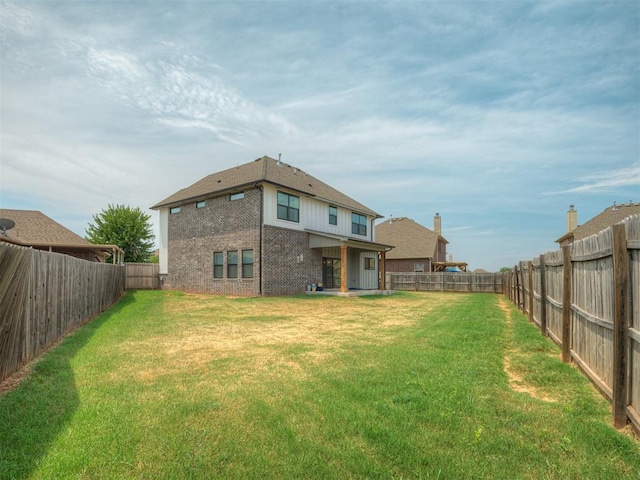 rear view of house featuring brick siding, a fenced backyard, and a lawn