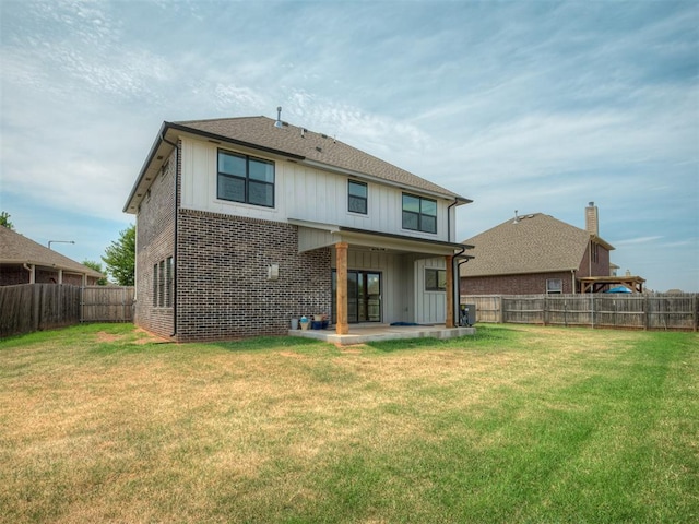 rear view of property with board and batten siding, a yard, a fenced backyard, and a patio area