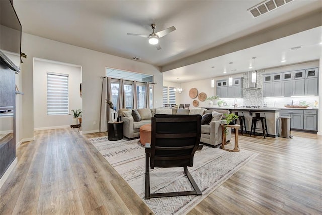 living area featuring baseboards, visible vents, light wood-style flooring, and ceiling fan with notable chandelier