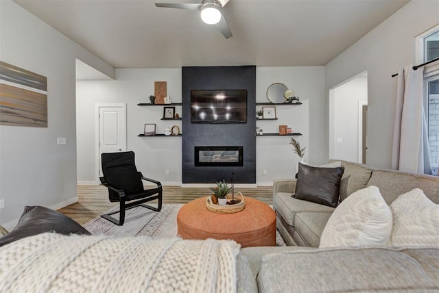 living area featuring baseboards, ceiling fan, a fireplace, and wood finished floors
