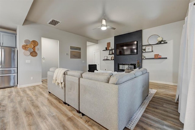 living room featuring baseboards, ceiling fan, visible vents, and light wood-style flooring